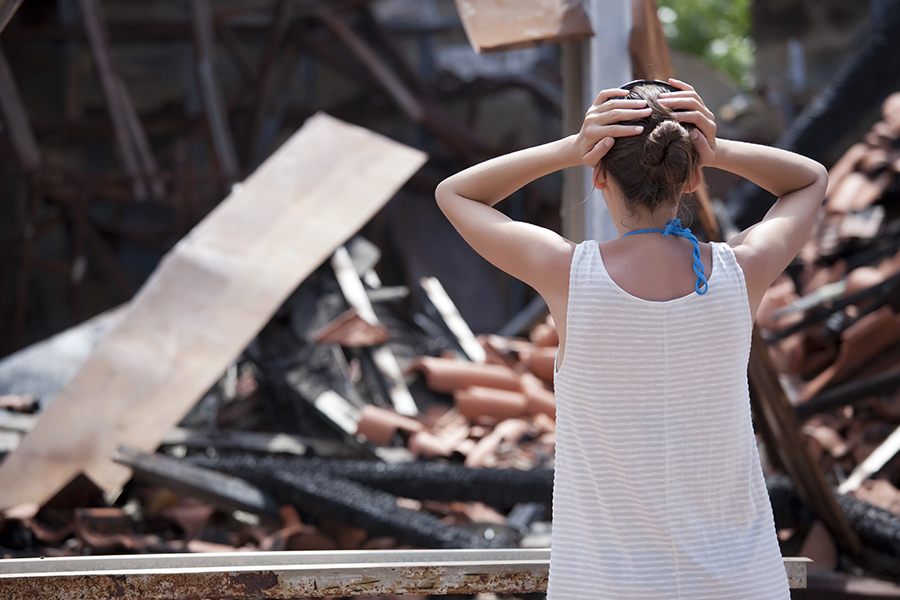 Insurance Tips, Difference in Conditions Insurance - Woman with Arms Raised Stands in Front of Her Storm Damaged Home